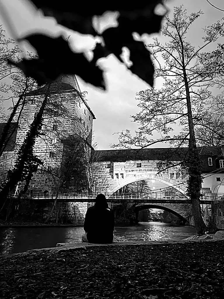 Puente iluminado en Nuremberg sobre un canal de noche con una persona sentada en primer plano, estilo monocromo