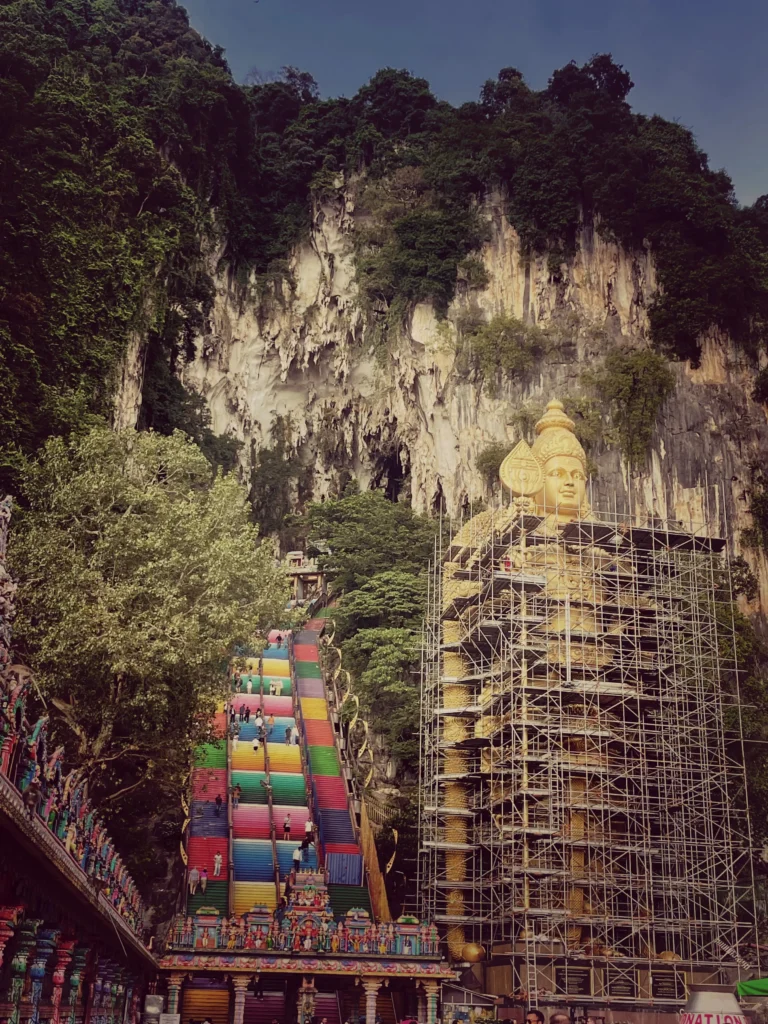 Vista de las escaleras de acceso a Batu Caves junto a la inmensa estatua dorada de Lord Murugan rodeada de andamios y en obras de mantenimiento.