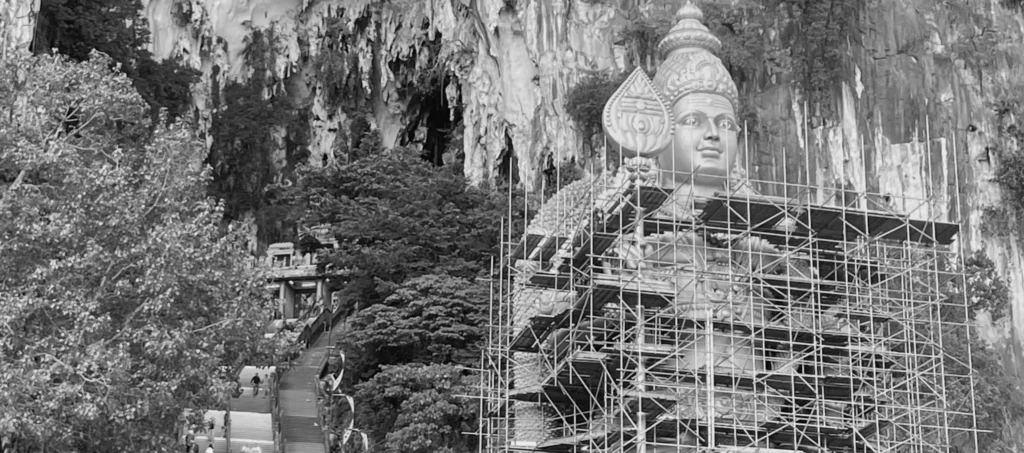 Fotografía en blanco y negro del rostro de la estatua de Lord Murugan y el tramo final de las escaleras de acceso a las cuevas de Batu.